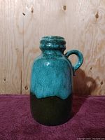 Front view of the Scheurich pottery jug vase showing the green drip glaze over black base with a single handle by the neck.