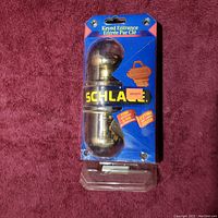 Front view of Schlage keyed entrance door knob in sealed packaging showing brand name, lifetime finish guarantee, and clear view of knob shape and finish.