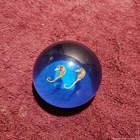 Top view of the acrylic spherical paperweight showing two gold-tone seahorses embedded inside a blue gradient background.