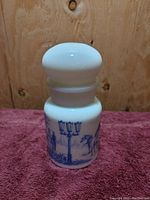 Front view of the milk glass spice jar showing blue patterned figures and lamp post on white glass, bubble lid prominently visible