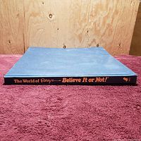 Side view of the spine showing the title 'The World of Ripley's Believe It or Not!' in orange text on a blue background.