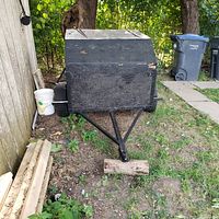 Front view of the black wooden enclosed trailer box with a metal frame and hitch, missing tire and lights.