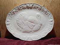 Front view of white ceramic turkey platter showing detailed embossed turkey in the center and decorative border with fruit and leaf motifs.