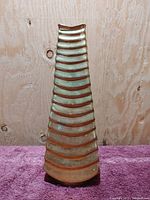 Front view of the vintage brass vase showing tall, tapered shape with horizontal ridged bands on a textured background.