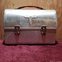 Front view of vintage American Thermos metal lunch box showing clips and raised emblem