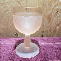 Front angle view of frosted light pink glass goblet showing floral embossed pattern and textured stem.