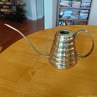Side view of the vintage brass watering can showing the ribbed body, long spout, and curved handle