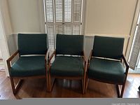 Front view of the 3 wooden framed chairs with green padded seats and backs, arranged side by side.