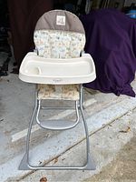 Photo of baby high chair with animal print padded seat, white plastic removable tray with cup holder, silver metal frame, footrest, and locking mechanism.