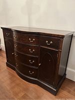 Photo of a solid wood buffet with dark finish, curved front, brass handles on drawers, and panel doors on sides.