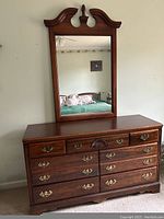 Front view of wooden bureau and attached mirror showing details of drawer handles, protective top coating, and decorative mirror frame.