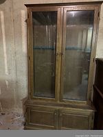 Front view of handmade wooden cabinet with glass upper doors and wooden lower doors, locks and key present.