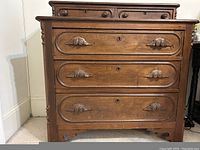 Front view of antique wooden bureau with three large drawers and two smaller drawers at top, showing carved wooden handles and keyholes.