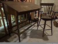 Wooden drafting table with angled top lid and matching swiveling chair in basement setting.