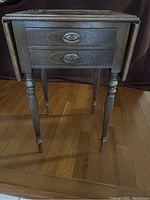 Front view of the antique wooden lamp table showing the front drawer with oval brass pulls and carved legs.