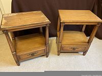 Pair of matching light brown wooden lamp tables shown front facing, highlighting top surface, shelf, and drawer. One table top shows wear and needs refinishing.