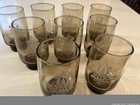 Nine brown medium-sized glasses with tan stencil floral design arranged in rows on table.