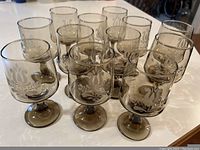 12 brown tinted stemmed wine/water glasses arranged closely in rows showing tan stencil floral design