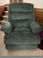 Front-facing image of large green overstuffed recliner showing cushioned armrests, padded backrest in three sections, and textured fabric upholstery.