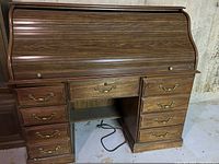 Closed roll top view of the wooden computer desk showing multiple drawers with brass handles and curved roll top cover.