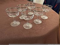 Six clear glass champagne coupe glasses with silver rims arranged on a textured brown surface.