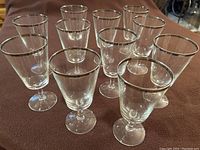 Eleven clear glass goblets arranged together showing their silver rims and stems.