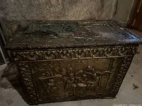 Front view showing embossed metal panel with figurative scene and floral border trim