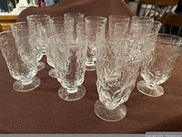 Photo showing 16 clear glasses with a wavy textured design, grouped closely together on a surface.