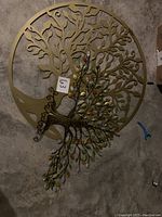 Large gold-tone circular tree cutout metal wall decoration with intricate branches and leaves design, placed on floor.