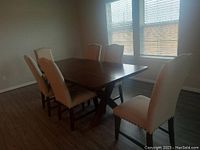Full set showing rectangular wood table with six beige upholstered chairs in a dining room setting near window.