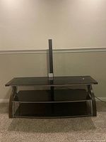 Front view of the tempered glass TV stand against a light wall, showing all three shelves and curved legs.