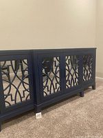 Front view of the blue TV stand showing four mirrored panel cabinet doors with geometric decorative front.