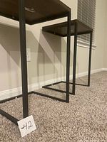Side view of two black metal frame side tables showing open rectangular legs and wood tops.