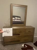 Two photos showing a wooden dresser with 7 drawers of varying sizes and a matching rectangular vanity mirror with a thick wooden frame. The dresser and mirror have a natural wood finish and simple design.