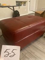 Side angle view of red leather ottoman showing tufted top and stitching detail.