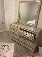 Photo showing 6 drawer dresser with vanity mirror on top, beige finish, metal handles, placed in bedroom setting.