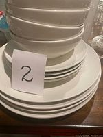 Stack of ivory white large and small plates with bowls on top. All items shown in good condition without visible damage.