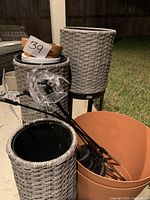 Photo showing three gray woven tall planters on stands, one large terracotta plastic pot, two small stacked terracotta pots inside one planter, and clear butterfly garden stakes with solar panels inside the large plastic pot.
