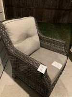 Side angled view of one wicker lawn chair showing armrest, woven frame, and beige cushion with button tuft.