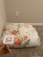 Pink and white floral comforter folded on carpeted floor, showing floral pattern and texture.