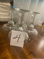 Four clear margarita glasses upside down on a wooden table showing stems and bases.