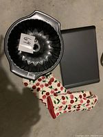 Bundt cake pan, cookie sheet, and cherry print oven mittens placed together on floor