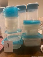 Multiple assorted plastic storage containers, mostly round and square shapes with blue lids, stacked neatly together
