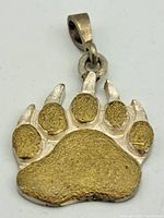 Front view of claw-shaped pendant with gold-tone paw pads and silver-tone claws, showing textured surface.
