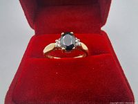 Front view of a yellow gold ring with a dark ocean blue oval sapphire in center and two small diamonds on sides, placed on red velvet background.
