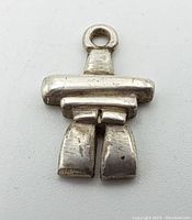 Close-up photo of the Inukshuk pendant showing its shape and metal texture with marks and wear.