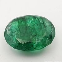 Close-up image of the 15.85CT oval cut emerald gemstone showing green color, faceted surface, and natural inclusions.