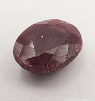 Close-up of the oval red ruby gemstone showcasing its deep red color and faceted cut with visible inclusions.