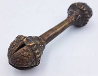 Close-up side view of the antique bronze rattle showing detailed floral embossed design and patina
