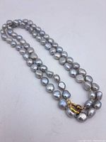Full view of the double strand black baroque pearl necklace laid flat showing pearls and gold-tone clasp.